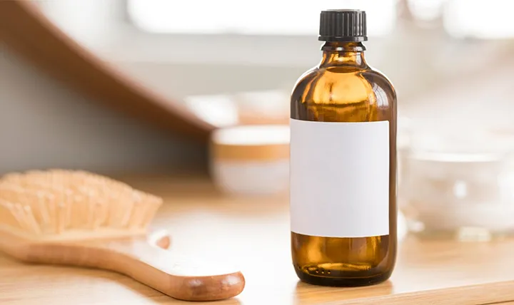 A brown amber bottle with a black cap and blank white label on a wooden table next to a brush.
